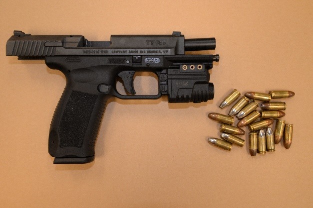 A black semi automatic handgun with an attached tactical light, placed next to a scattered group of brass colored bullets on a tan background