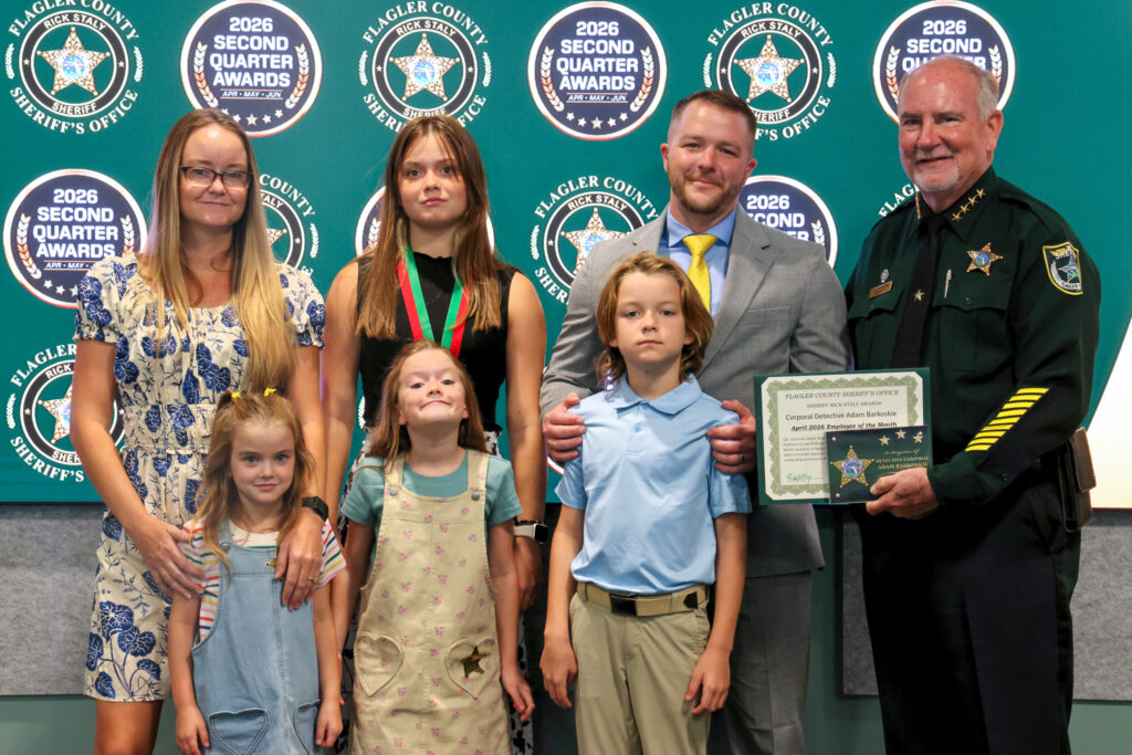 A family and a Flagler County sheriff pose at an awards ceremony The sheriff holds a certificate There are event logos in the background The group includes three children, two women, and a man in a suit