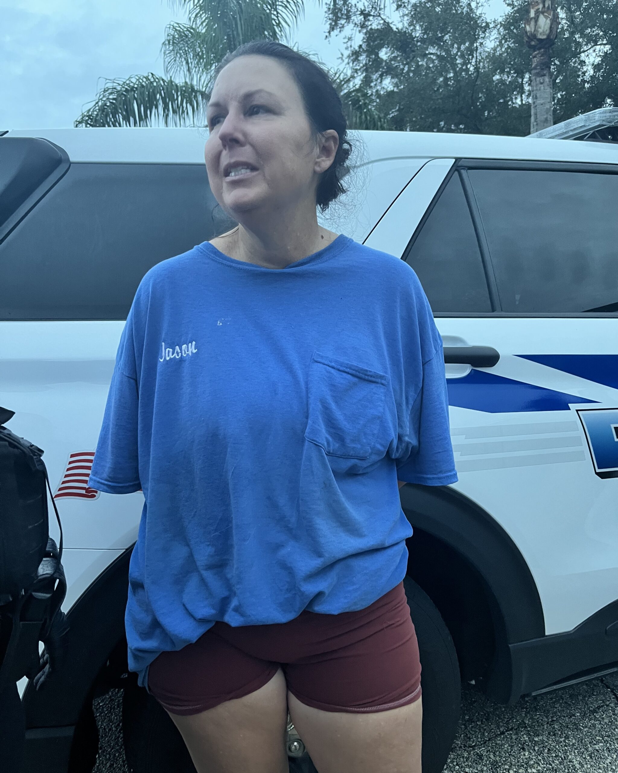 A woman wearing a blue t shirt with “Jason” embroidered on the chest stands in front of a white police vehicle